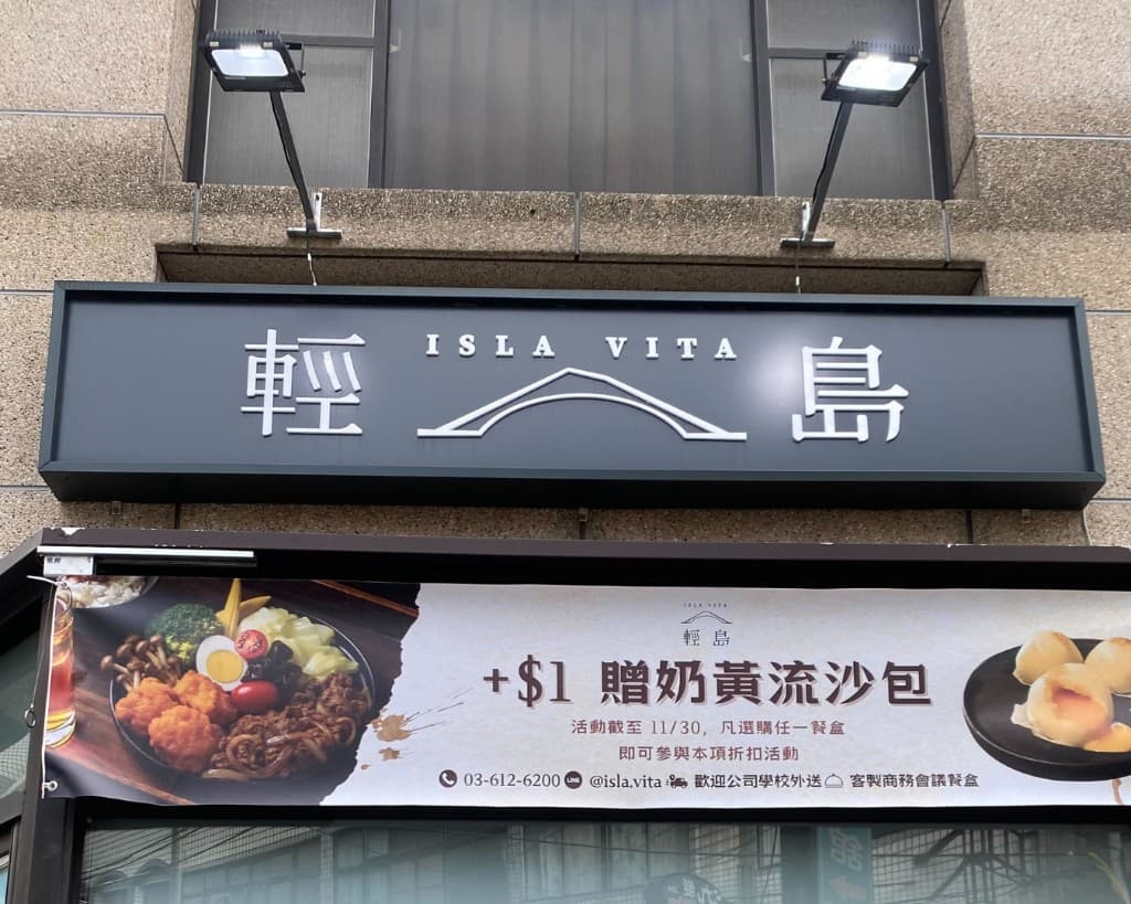 輕島 ISLA VITA 店招與橫幅：石牆上的黑色招牌與白色餐盒促銷橫幅、餐點照片